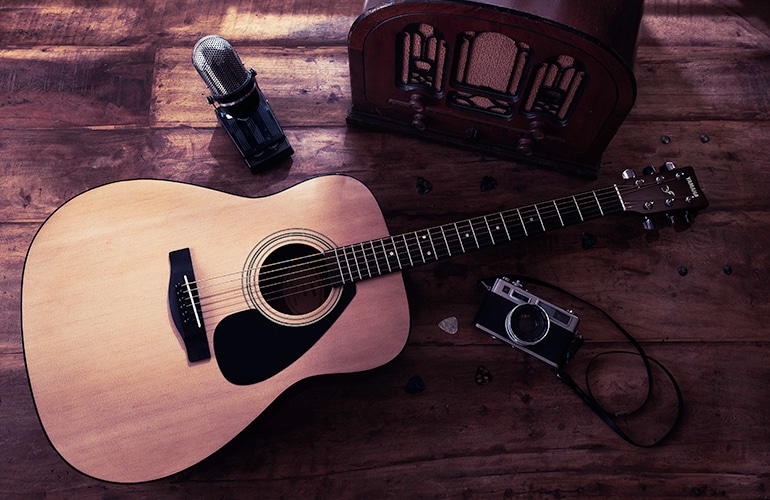 F310 Natural acoustic guitar on the floor with a guitar pick, microphone, vintage camera and jukebox.