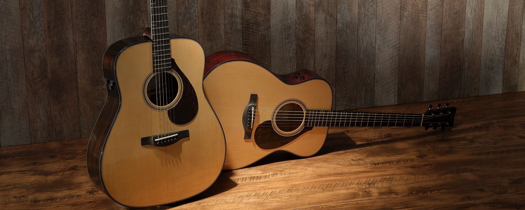 A FG9 RX and a FS9 MX are lined up on a wooden floor, showcasing the differences in their body shapes and types of wood used. The FG9 RX is standing upright on the left, while the FS9 MX is lying down on the right.