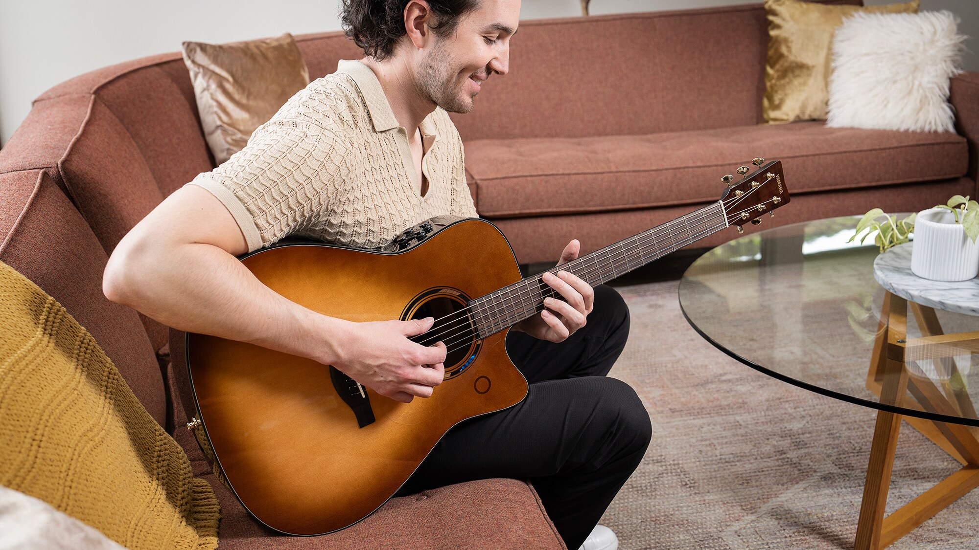 Un homme assis sur un canapé dans le salon jouant d'une guitare acoustique TAG3 C