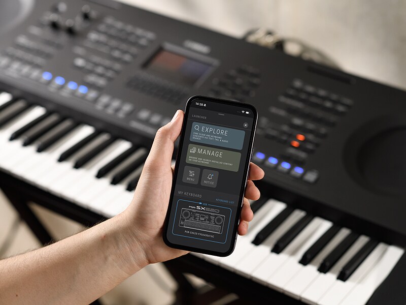 Le PSR-SX920 et une main tenant un smartphone affichant un lecteur de musique.