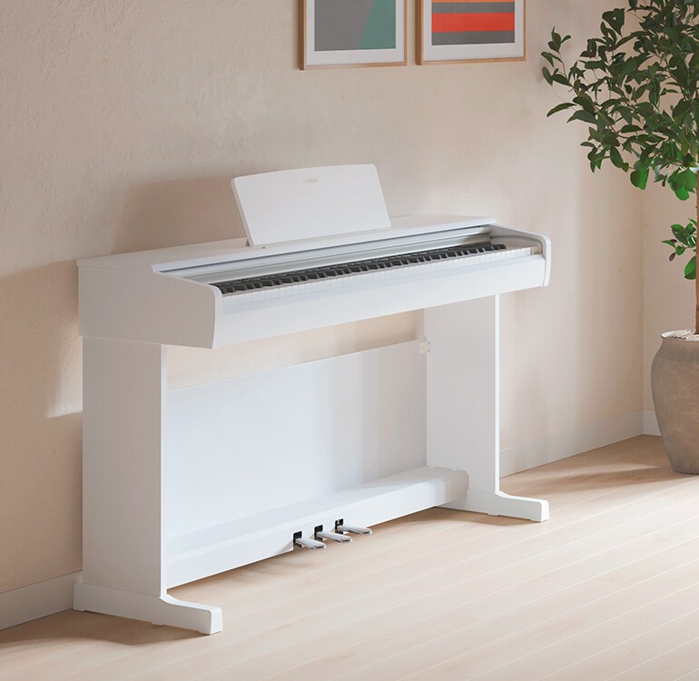 Un salon accueillant un piano ARIUS blanc avec des plantes d'intérieur et un canapé, s'intégrant harmonieusement à la décoration.