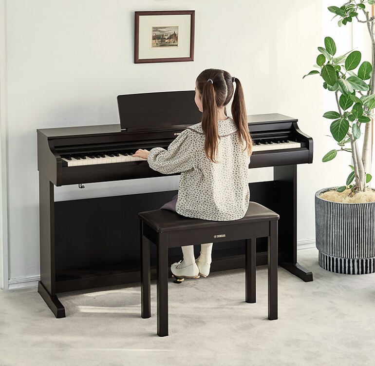 Une jeune fille s'exerçant sur un piano ARIUS dans un salon.