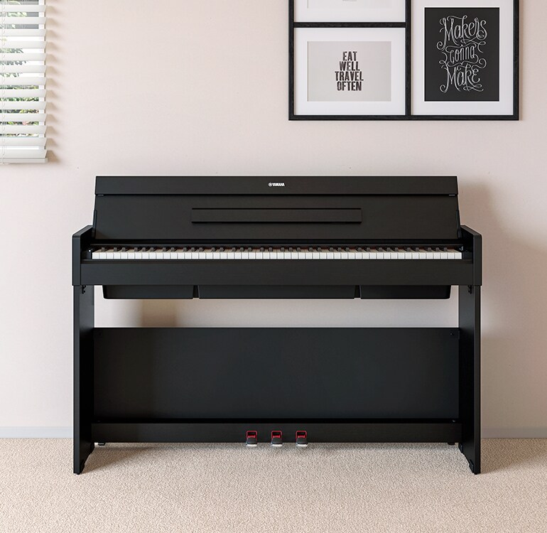 Un salon accueillant un piano ARIUS noir placé à côté d'étagères murales sur lesquelles sont disposés des lampes et un diffuseur, s'intégrant harmonieusement à la décoration.
