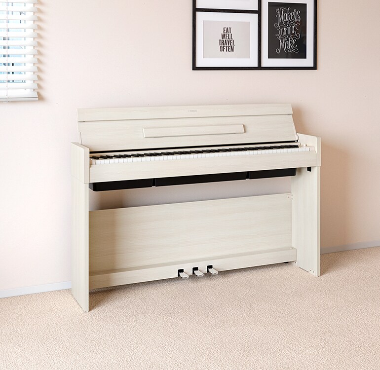 Un salon accueillant un piano ARIUS bouleau blanc placé à côté d'étagères murales sur lesquelles sont disposés des lampes et un diffuseur, s'intégrant harmonieusement à la décoration.