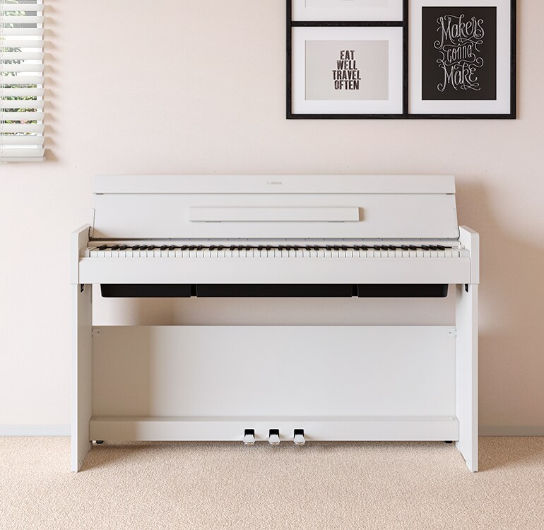 Un salon accueillant un piano ARIUS blanc placé à côté d'étagères murales sur lesquelles sont disposés des lampes et un diffuseur, s'intégrant harmonieusement à la décoration.
